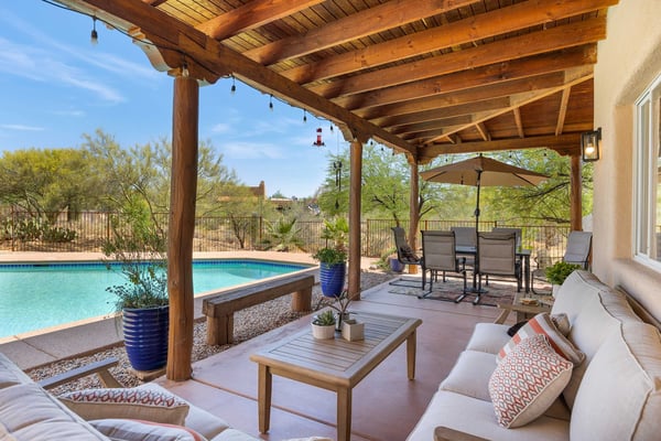 Covered patio with wooden beams, lounge seating, and view of swimming pool and desert landscape